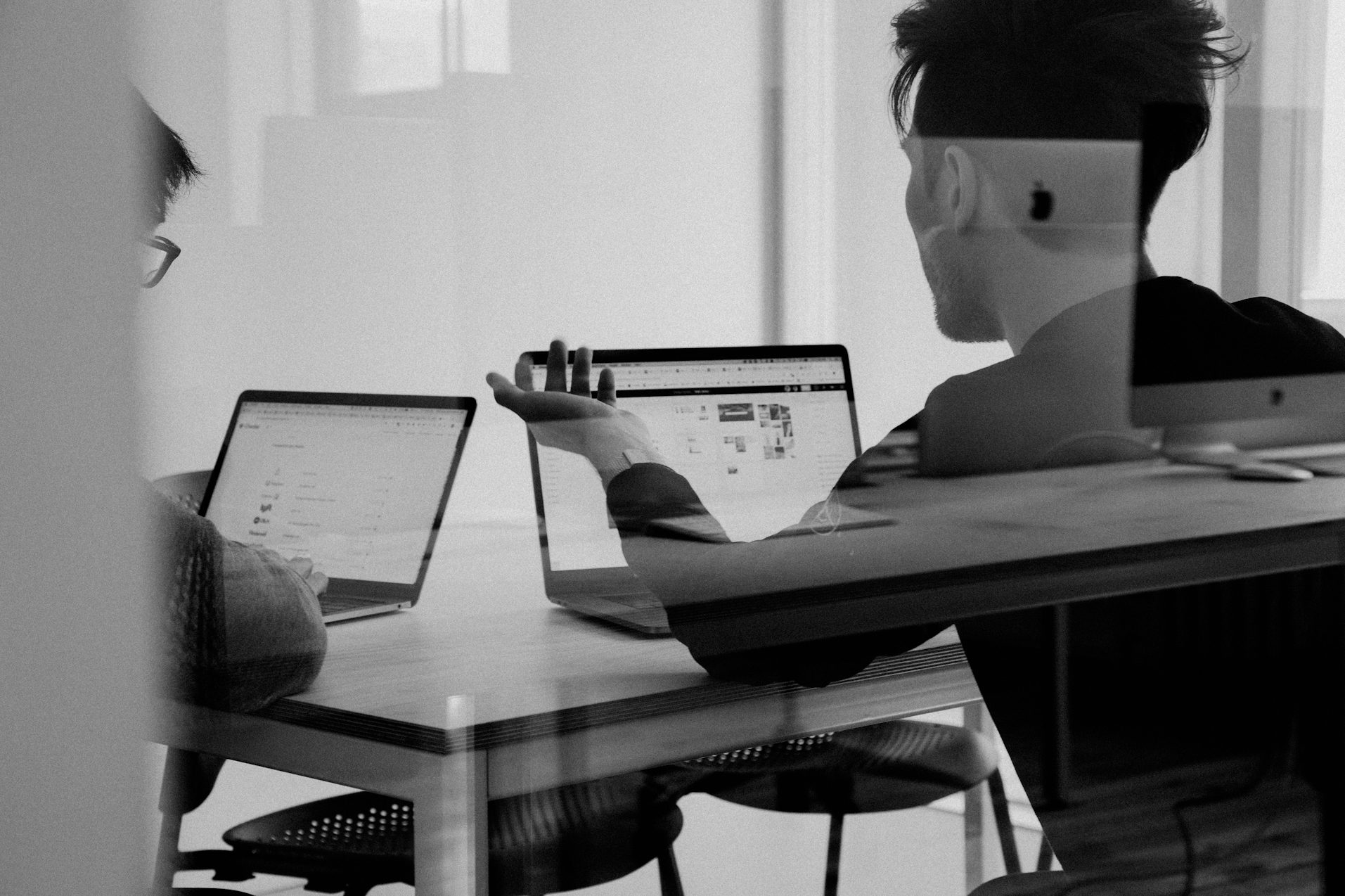 Zwei Personen sitzen am Tisch und arbeiten an Laptops in einem modernen Büro.
