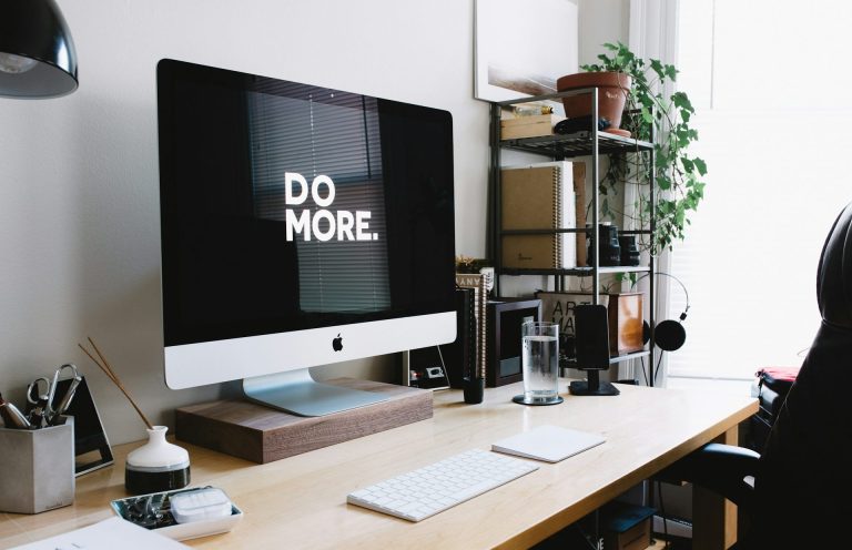 Schreibtisch mit Computer und der Aufschrift „DO MORE“ im Hintergrund.