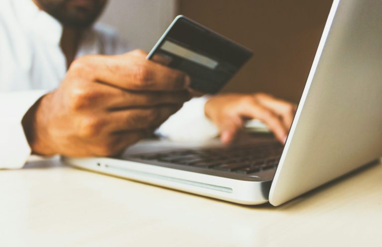 Eine Person hält eine Bankkarte und tippt auf einem Laptop.